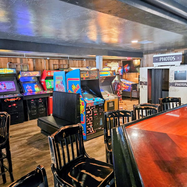 Arcade room with various classic game machines, a photo booth, and bar seating.