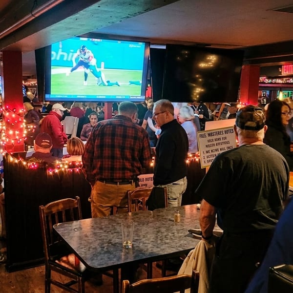 A lively bar scene with patrons watching sports on multiple large screens and mingling.