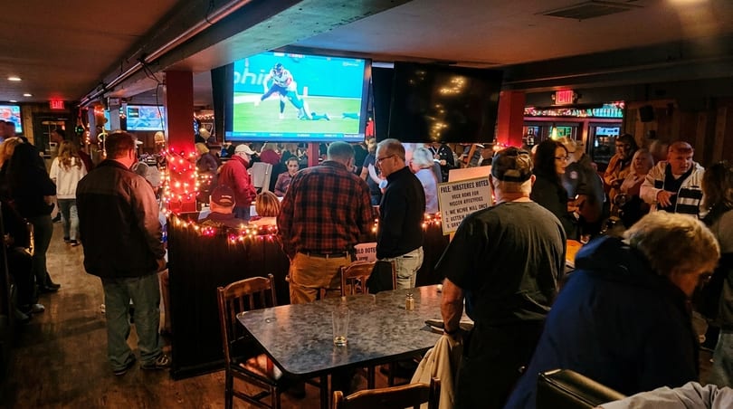 A lively bar scene with patrons watching sports on multiple large screens and mingling.