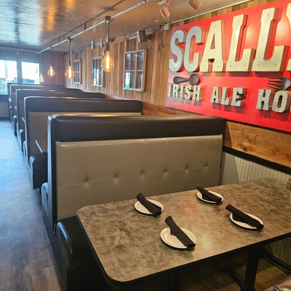 Restaurant interior with rows of booths, tables set with plates and napkins, and a large "SCALLY IRISH ALE HO" sign.