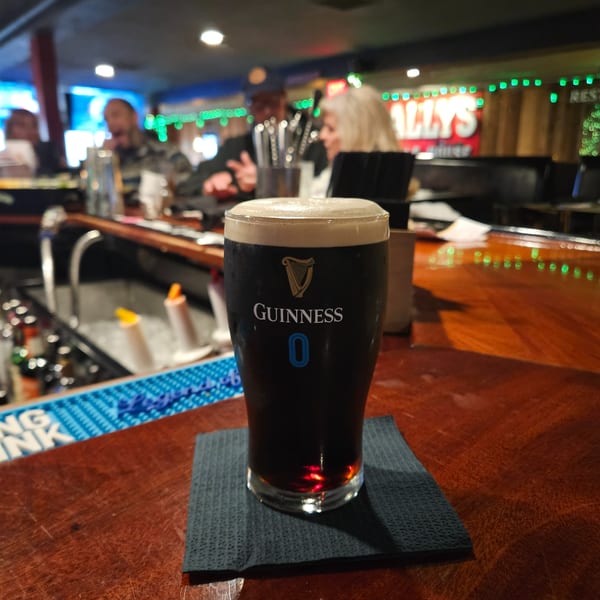 A pint of Guinness beer on a bar counter with people and green lights in the background.