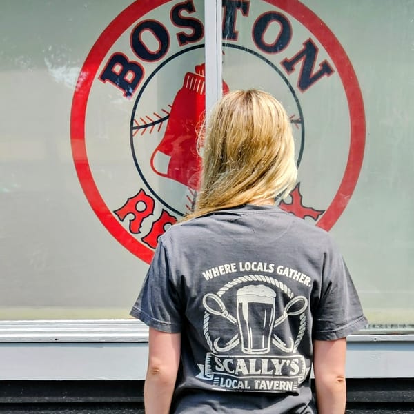 Blonde woman in a Scally's Local Tavern t-shirt looking at a Boston Red Sox logo.