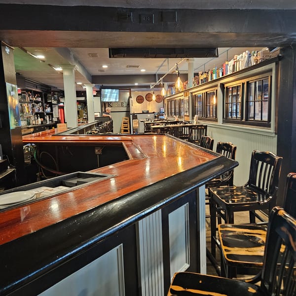 A long, polished wooden bar with black trim and bar stools in a dimly lit restaurant.