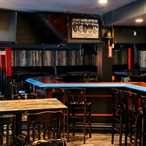 Interior of a dimly lit bar with a long wooden counter, bar stools, and tables.