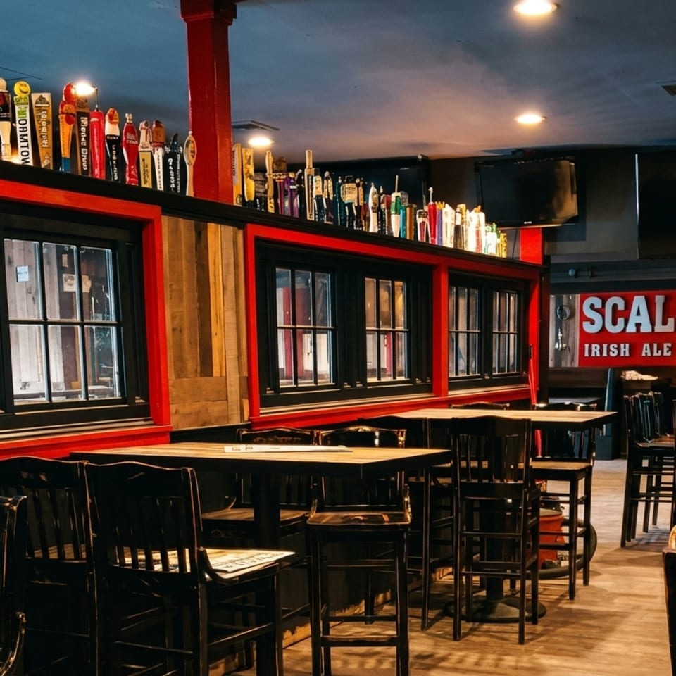 Interior of Scally's Irish Ale House, featuring tables, chairs, and a bar with many beer taps.