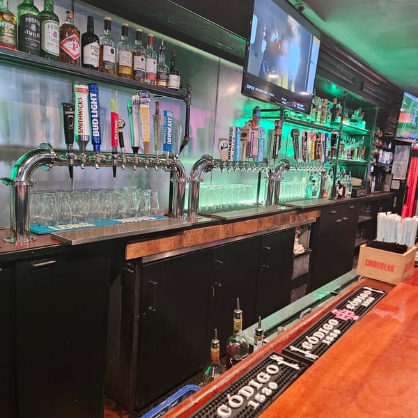 A well-stocked bar with numerous beer taps, liquor bottles, and glowing green shelves.
