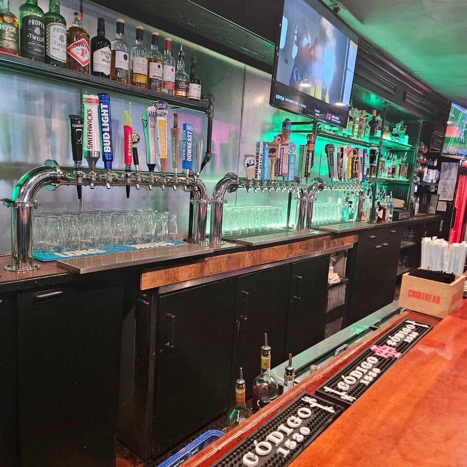 A well-stocked bar with numerous beer taps, liquor bottles, and glowing green shelves.