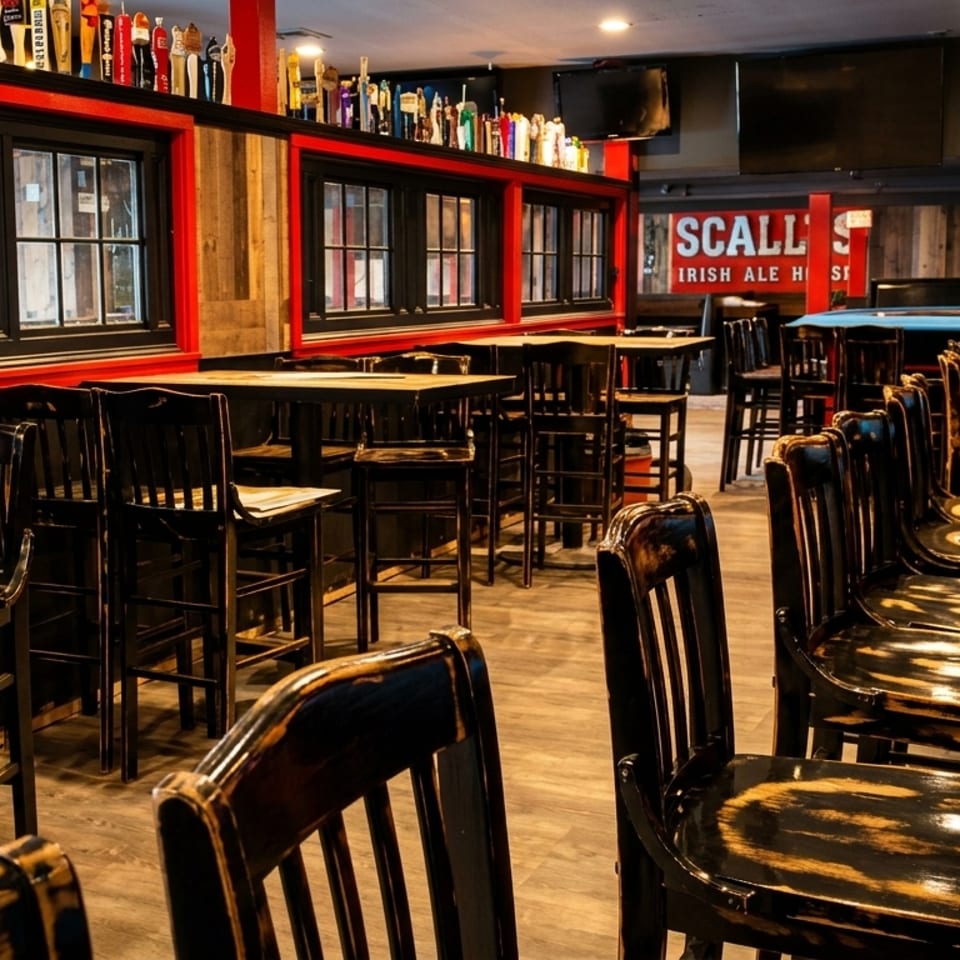 Interior of a pub with high-top tables, bar stools, and a long wooden bar.