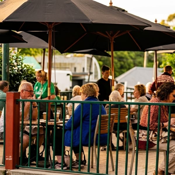 Patrons seated at outdoor tables under black umbrellas, enjoying a sunny day at a restaurant.