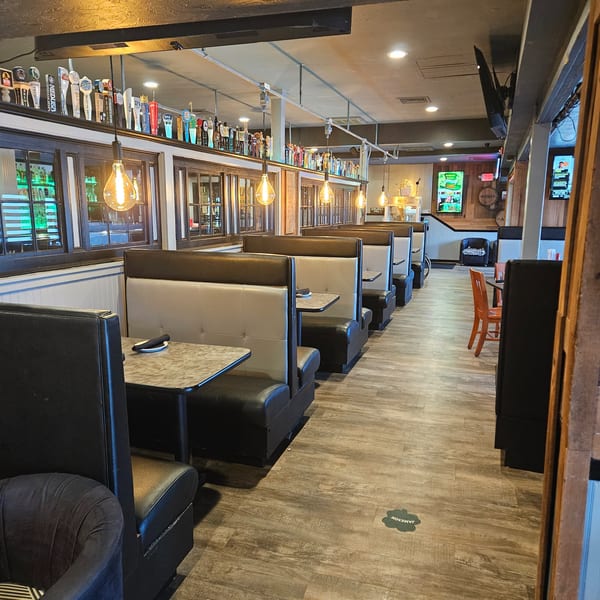 Restaurant interior with rows of empty booths, Edison bulb lighting, and a bar with many beer taps.